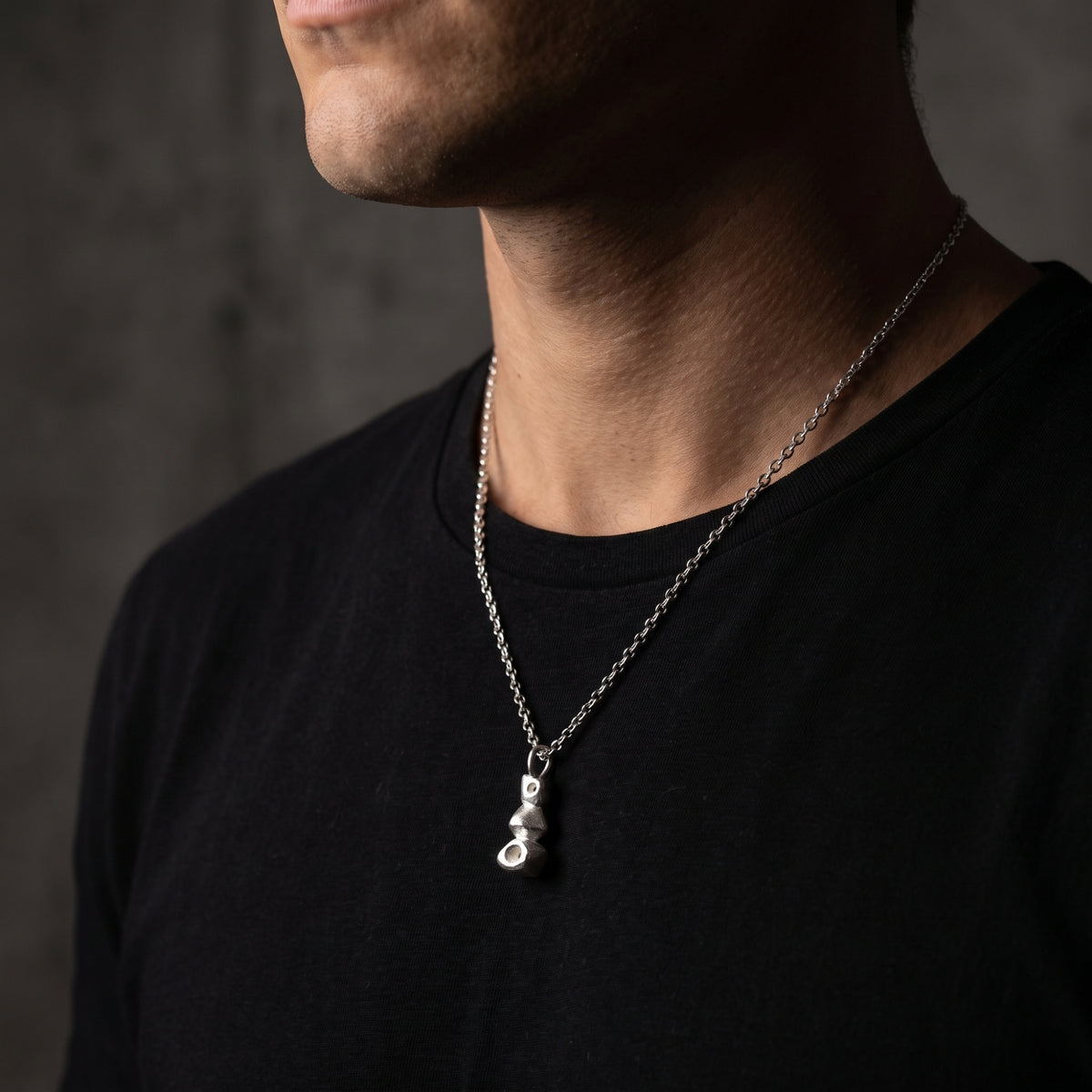 Side view of a man wearing the silver cairn pendant necklace over a black T-shirt.