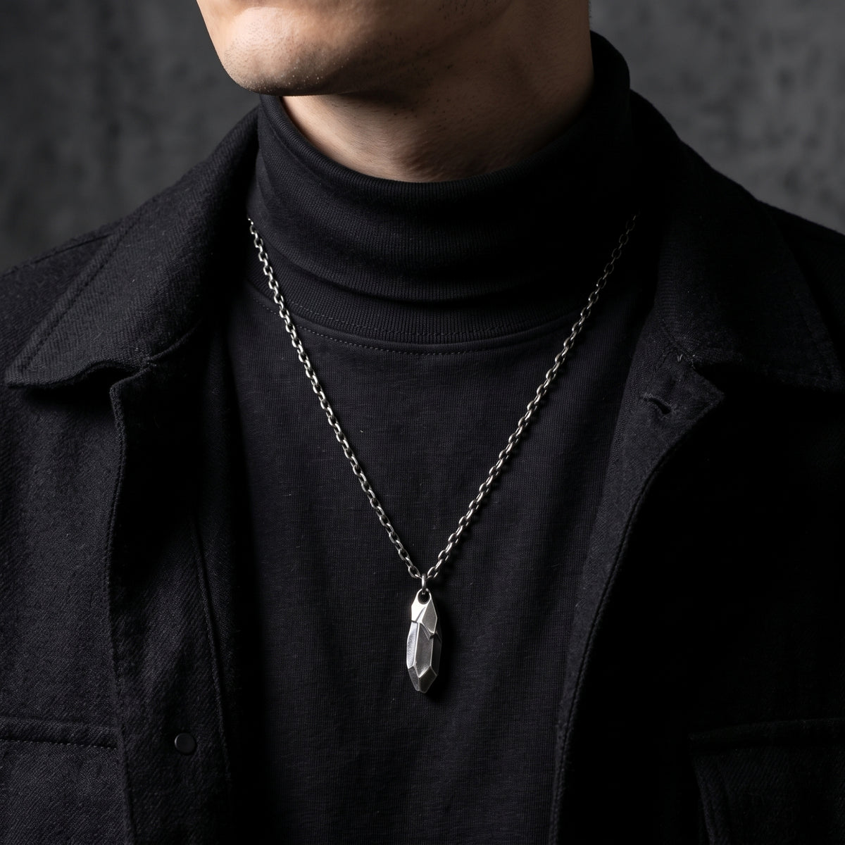 Faceted silver shard pendant worn over a black turtleneck and jacket.