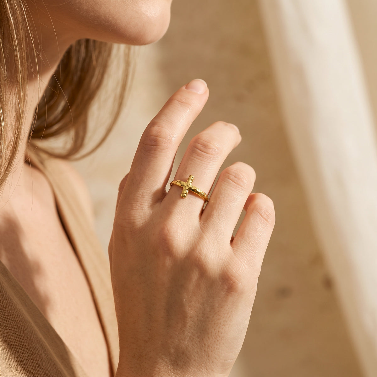 Close-up of a hand wearing the gold-tone hammered cross ring beside the model’s face.