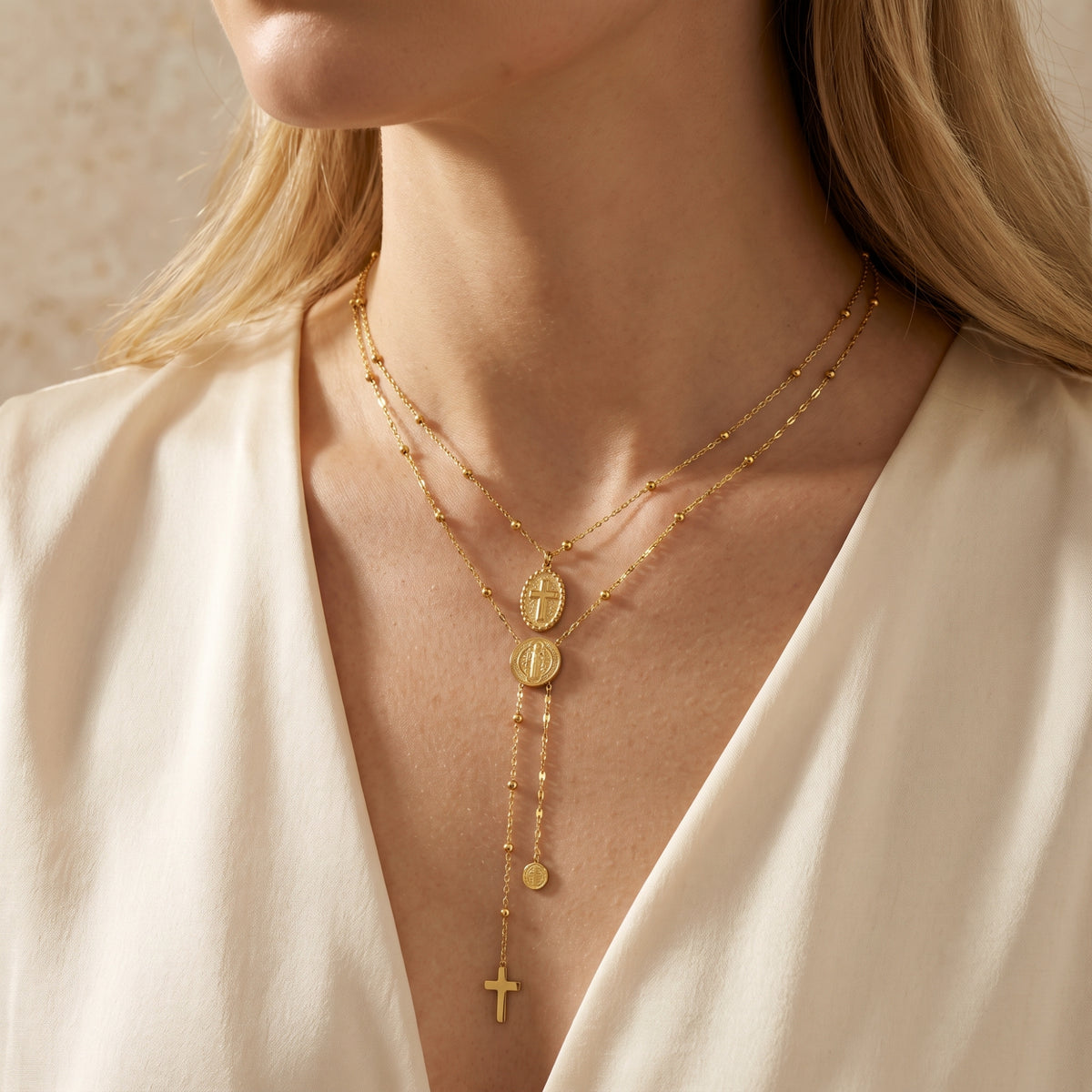 Model wearing the gold-tone layered necklace with oval cross and round medal over a white V-neck blouse