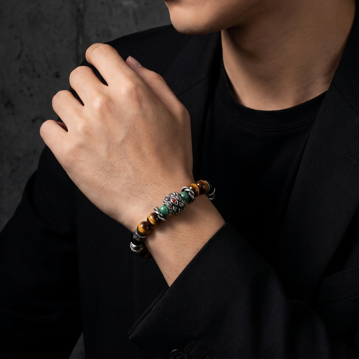 Model wearing a silver and tiger's eye beaded bracelet on his wrist against a black suit jacket.