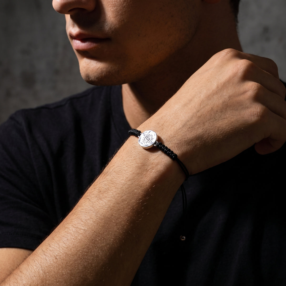 Model wearing the black cord bracelet with a central silver sun medallion on his wrist.