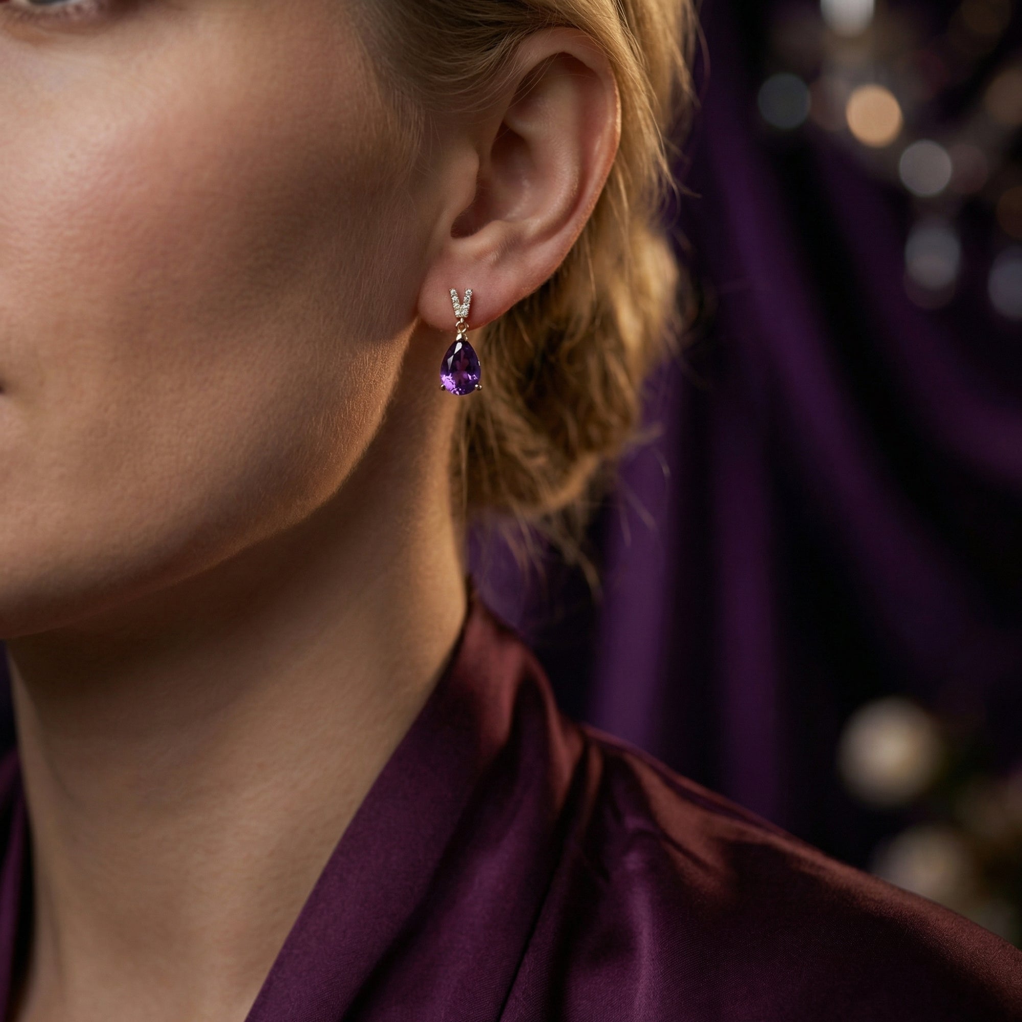 Model wearing a pear cut amethyst and 18k rose gold drop earring with a diamond-set bale.