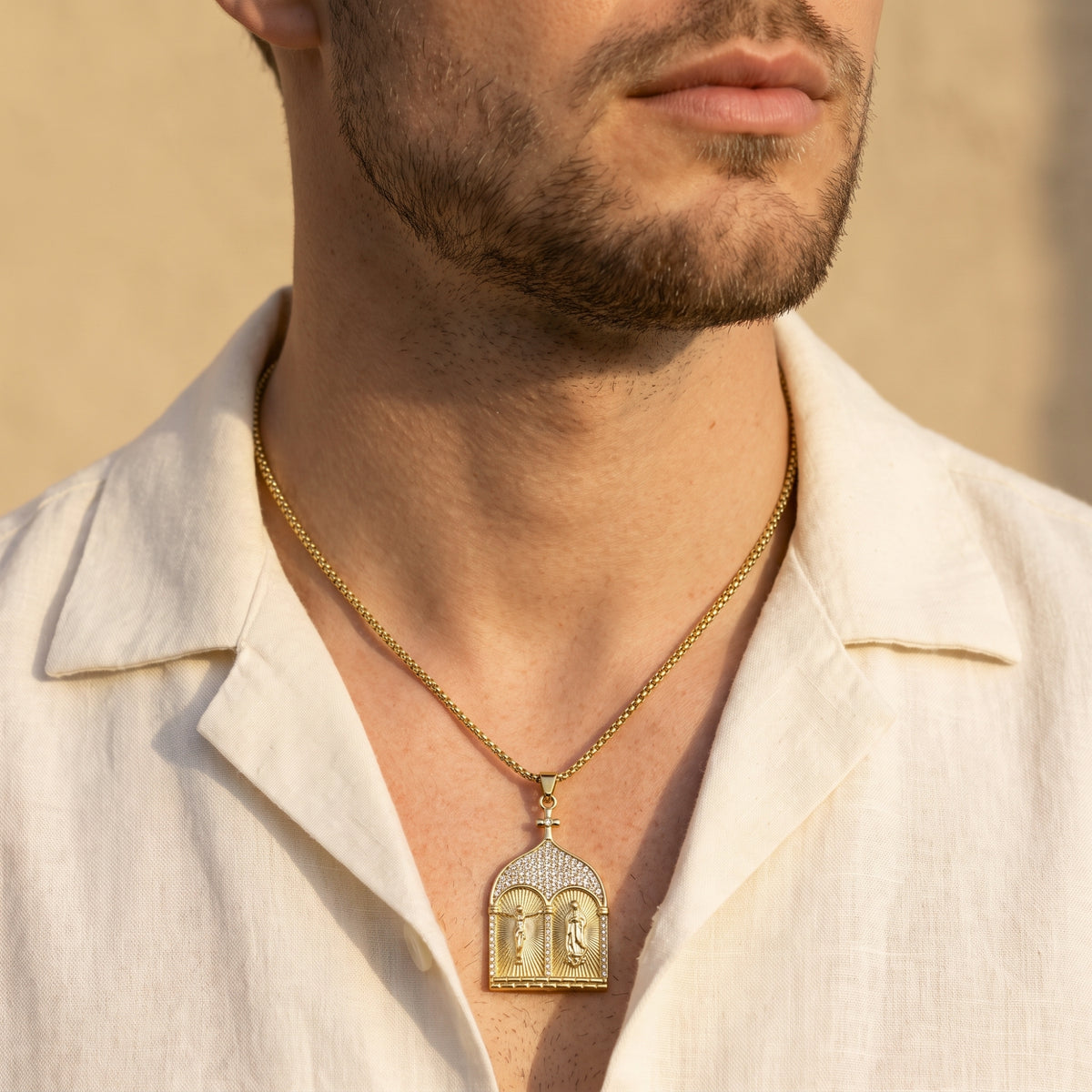 Front view of a man wearing the gold-tone diptych pendant necklace over an open white shirt.