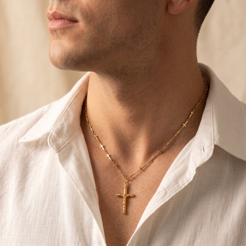 Close-up side view of a man wearing the gold-tone station crucifix necklace with an open white shirt.