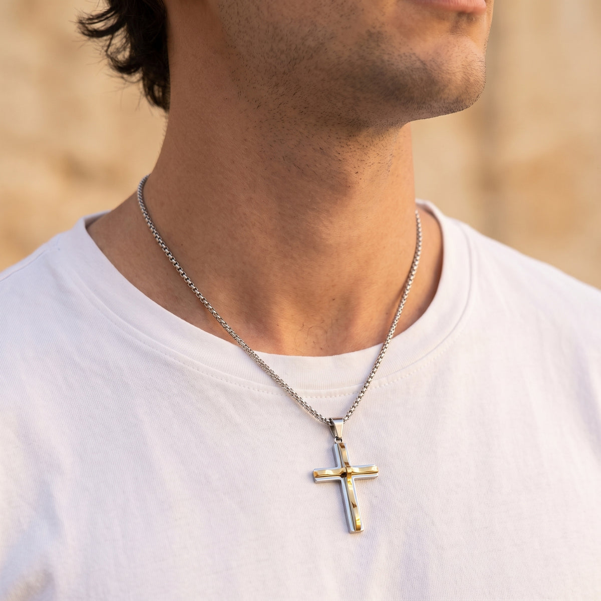 Man wearing the two-tone silver and gold-tone cross necklace over a plain white T-shirt.