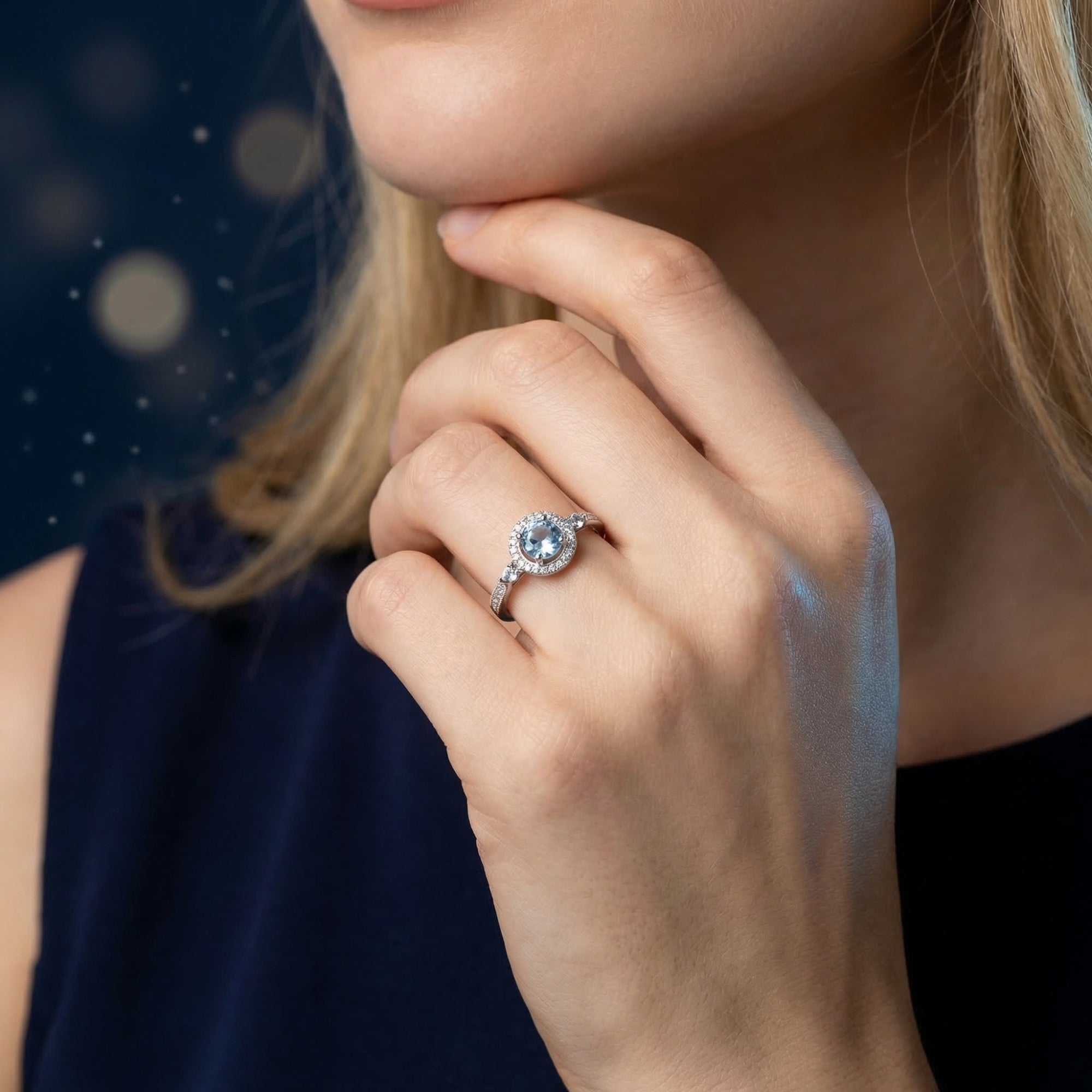 Woman wearing the Amabel round cut blue topaz silver ring on her ring finger, hand resting on her chin.
