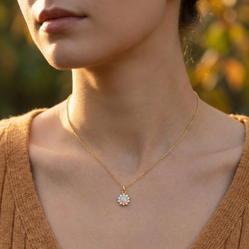 Model wearing the gold-tone Celestria round white opal pendant necklace against a soft outdoor background.