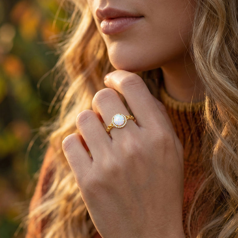 Model wearing the gold-tone Aureoline white opal statement ring on her finger in a natural outdoor setting.