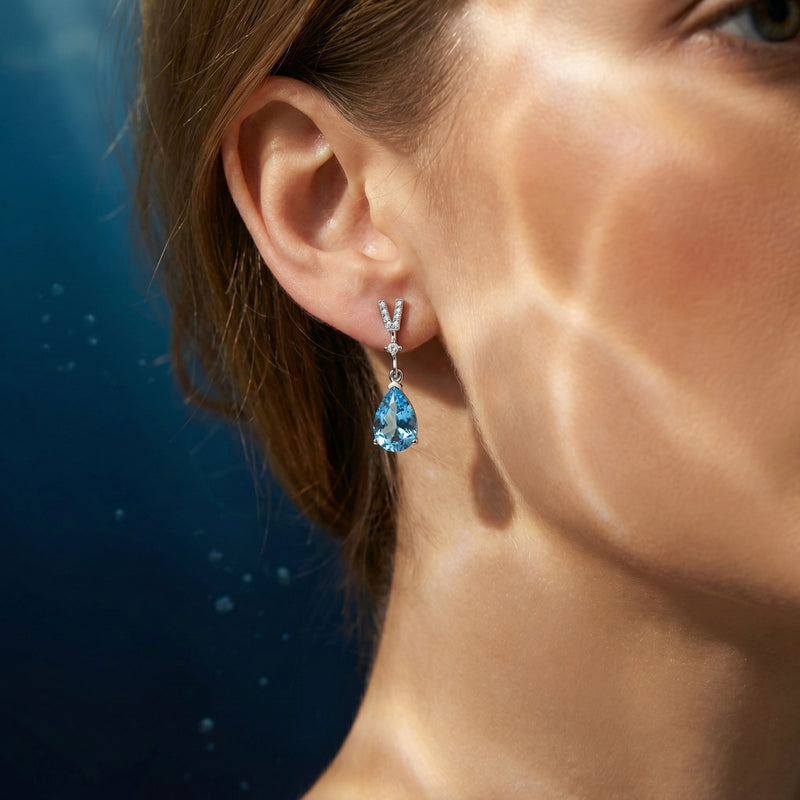 Model wearing a pear-cut aquamarine drop earring in platinum, highlighting the elegant dangle and blue stone.