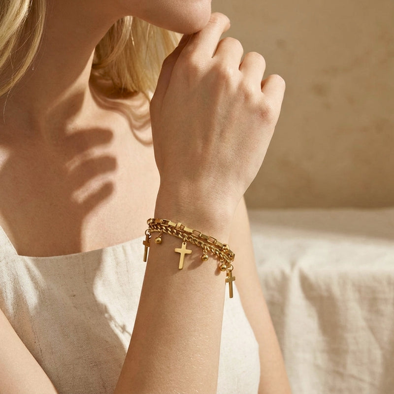 Close-up of a model wearing the gold-tone layered cross and bead charm bracelet with her hand raised to her chin.