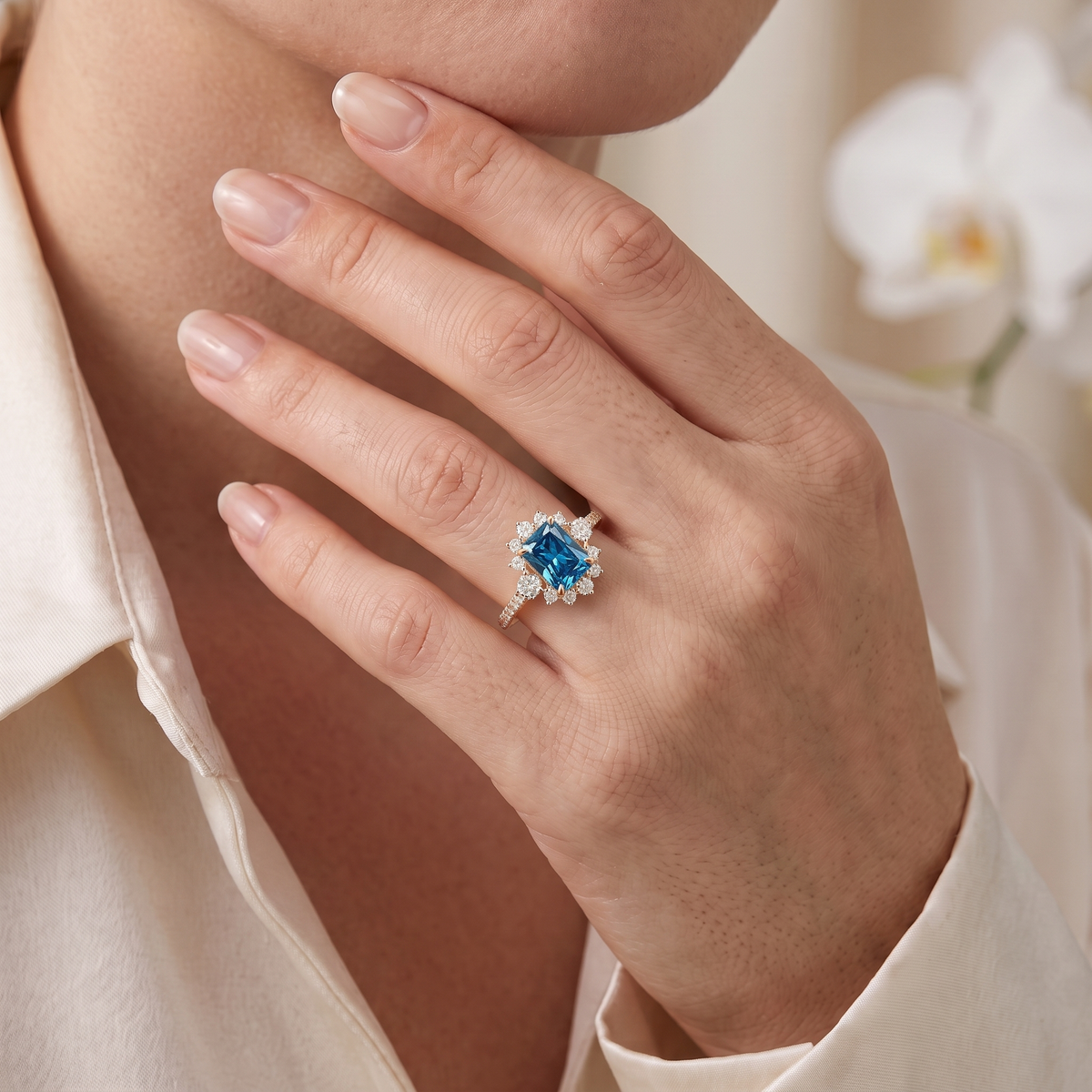 Close-up of rose gold radiant-cut blue moissanite halo engagement ring worn on model's hand.