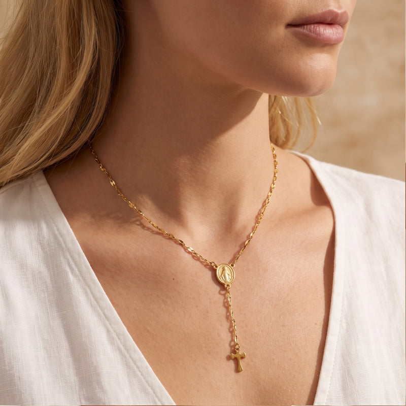 Angled side view of a model wearing the gold-tone rosary station cross necklace over a white top.