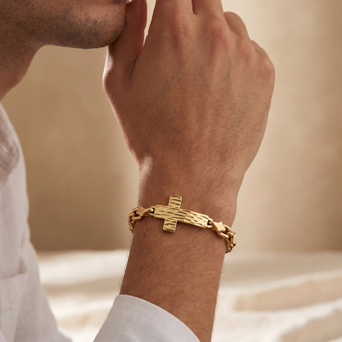 Gold-tone textured cross link bracelet worn on a man's wrist as he holds his hands near his chin.