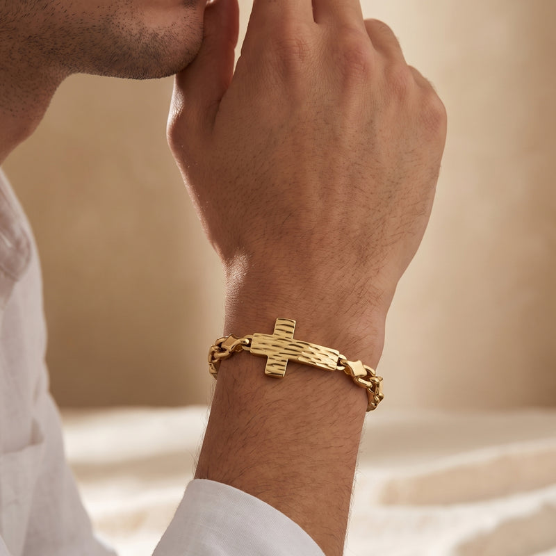 Gold-tone textured cross link bracelet worn on a man's wrist as he holds his hands near his chin.