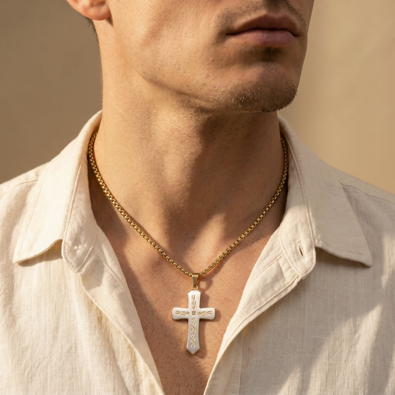 Man wearing a two-tone cross pendant on a gold-tone box chain with an open-collar cream shirt.