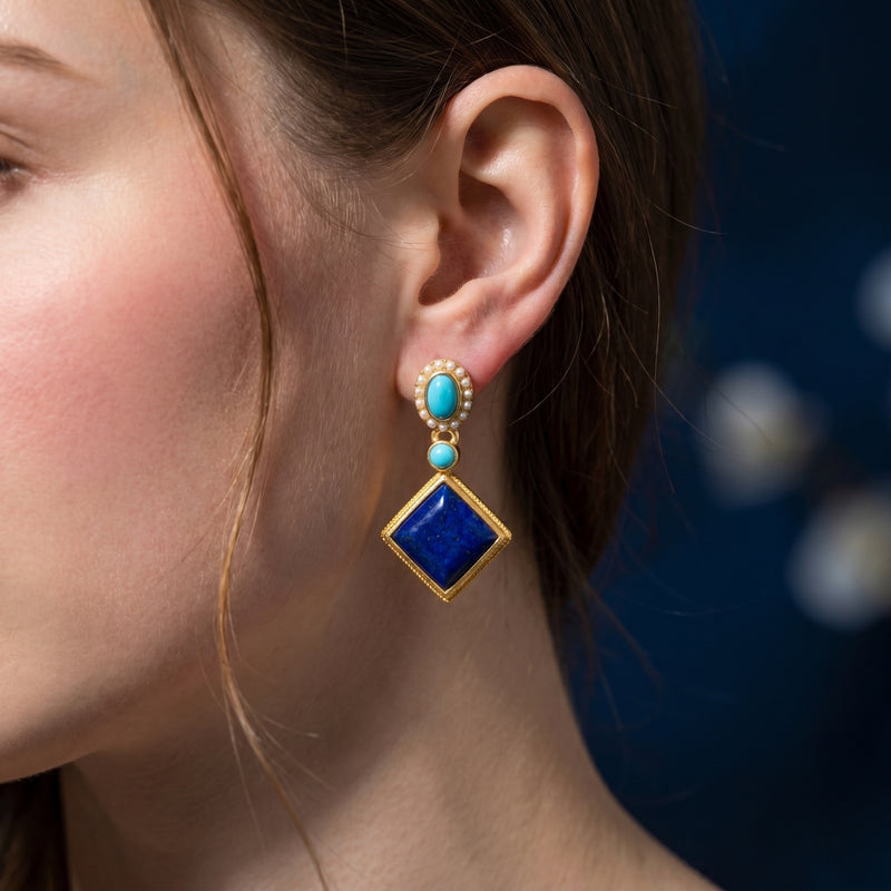 A model wearing the gold plated Azure Rhombus lapis earring featuring turquoise accents and a pearl halo.