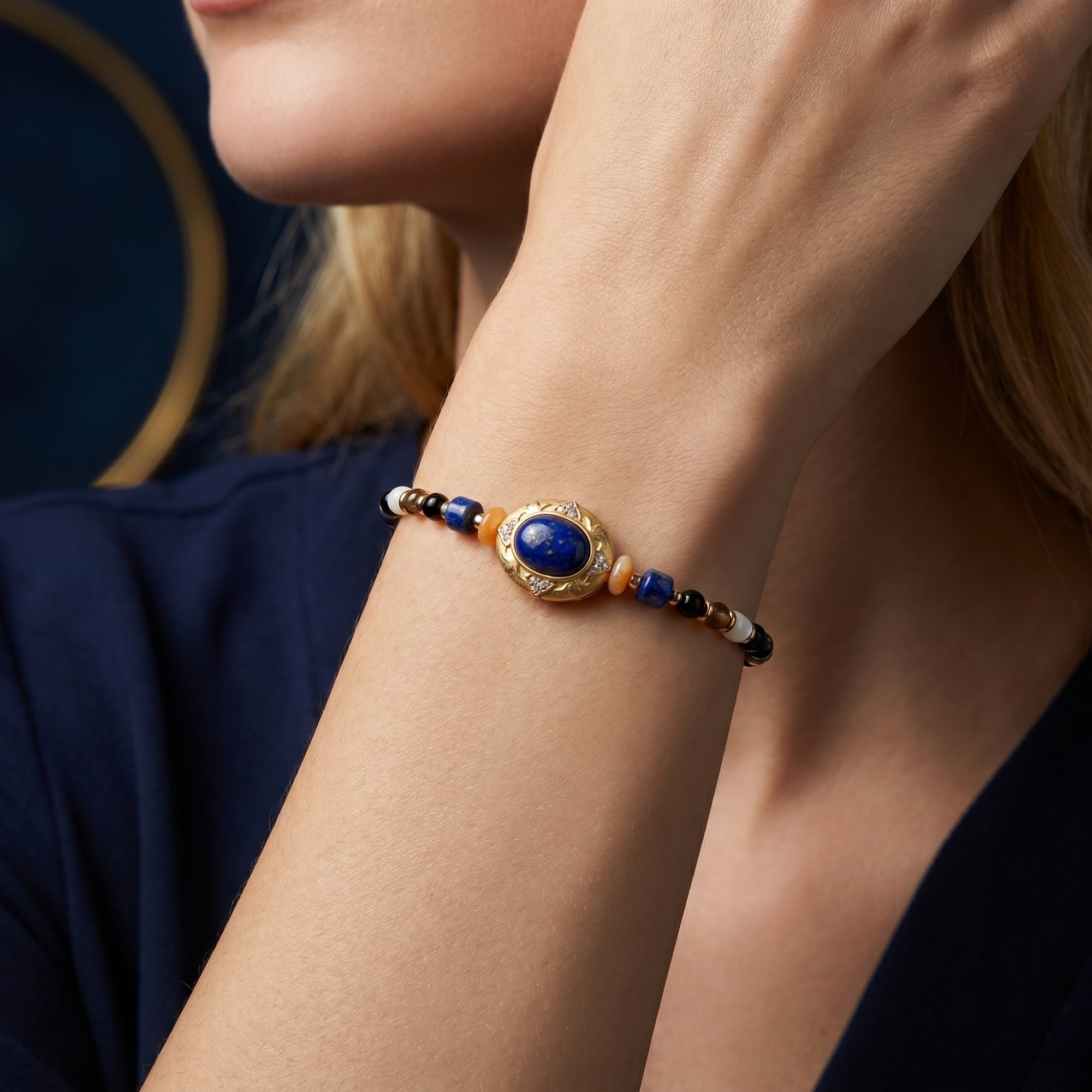 Gold-plated lapis lazuli bead bracelet worn on a woman's wrist, featuring a central oval lapis cabochon.