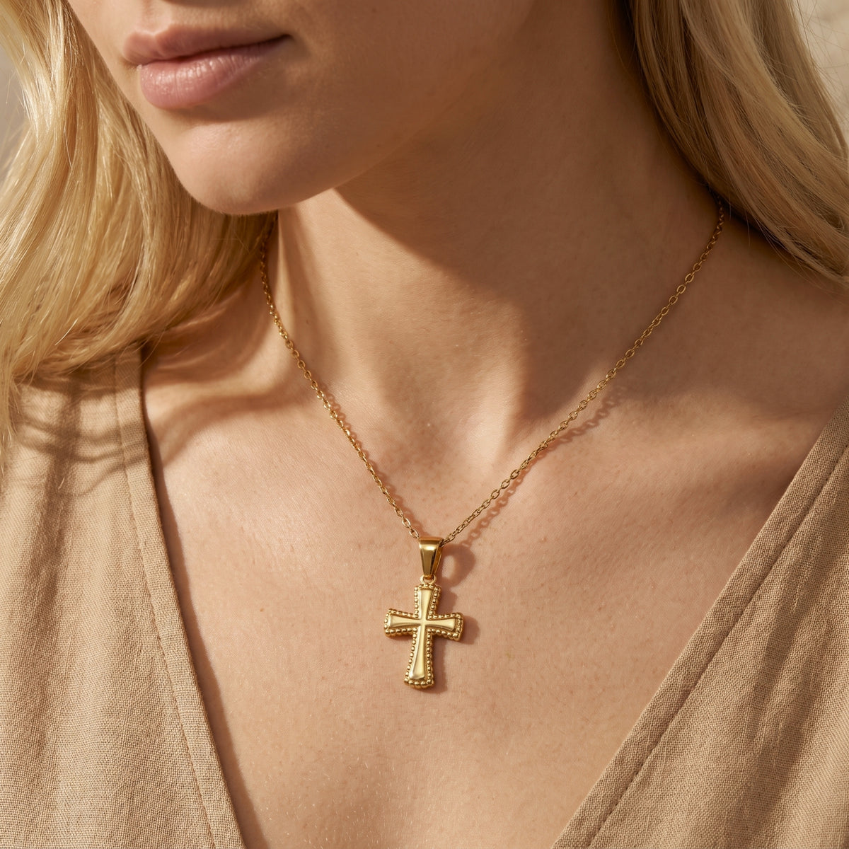 Gold-tone cross pendant necklace with a beaded border worn against a tan top.