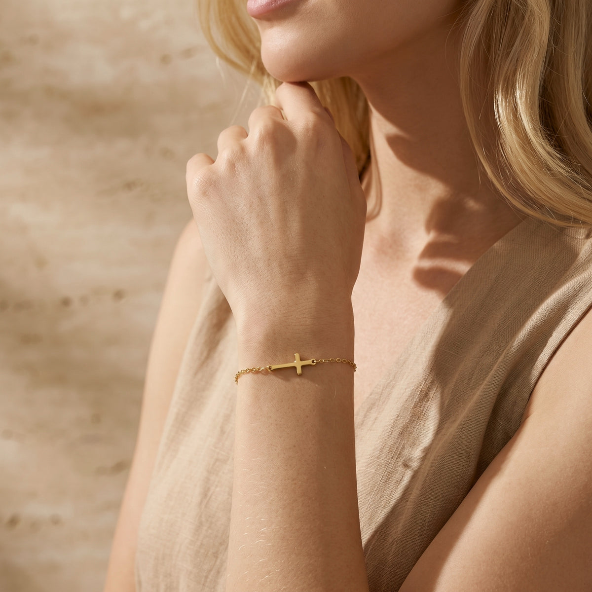 Model wearing a gold-tone horizontal cross bracelet on her wrist, with her hand raised near her chin.