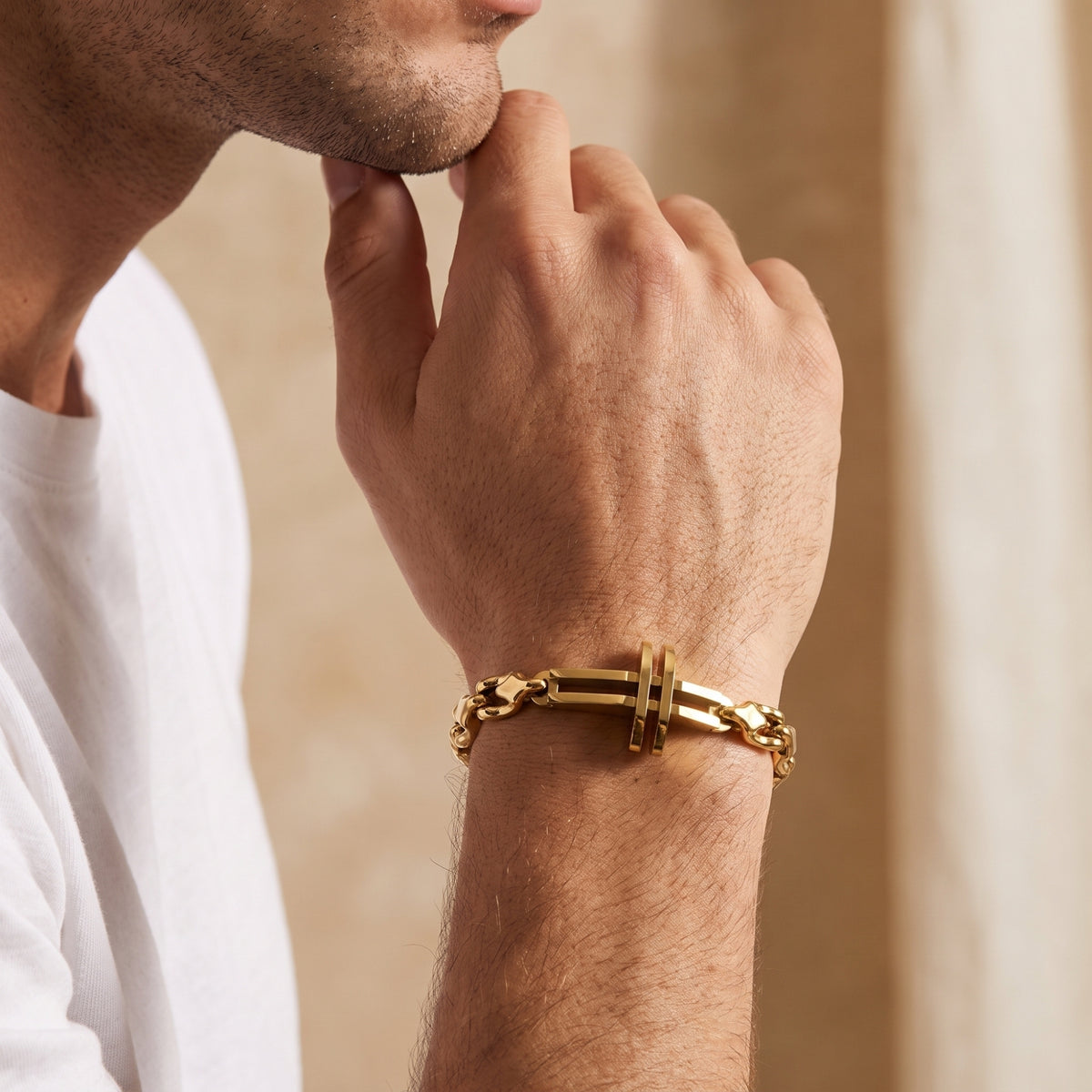 Man wearing the gold-tone cross link bracelet on his wrist with his hand near his chin.