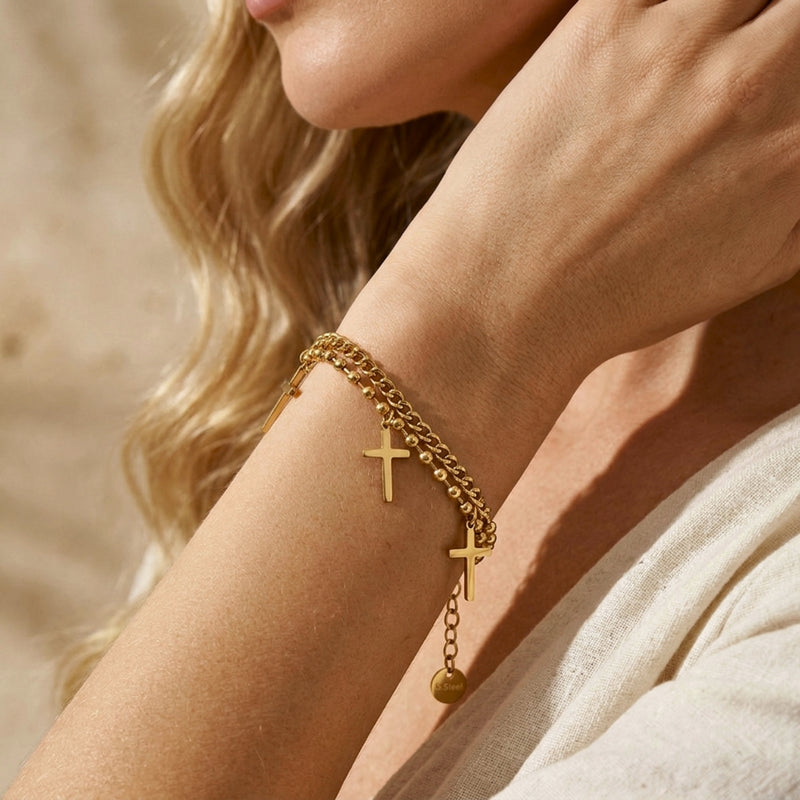 Close-up of a person wearing the gold double-strand bracelet, with two cross charms and an extender chain visible.