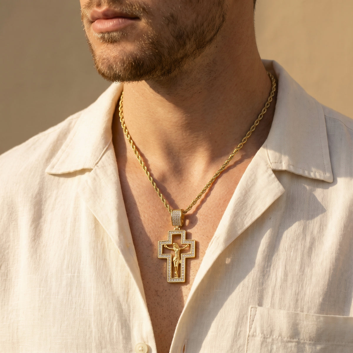 Man wearing a gold-tone cutout crucifix necklace over an open cream collared shirt.