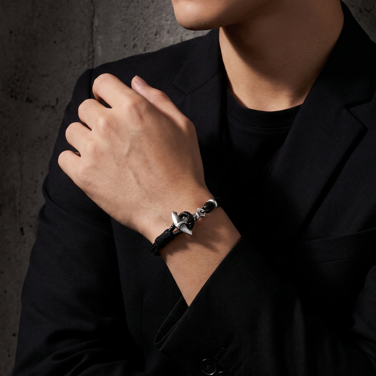 Man in a black blazer wearing a black cord anchor bracelet on his wrist.