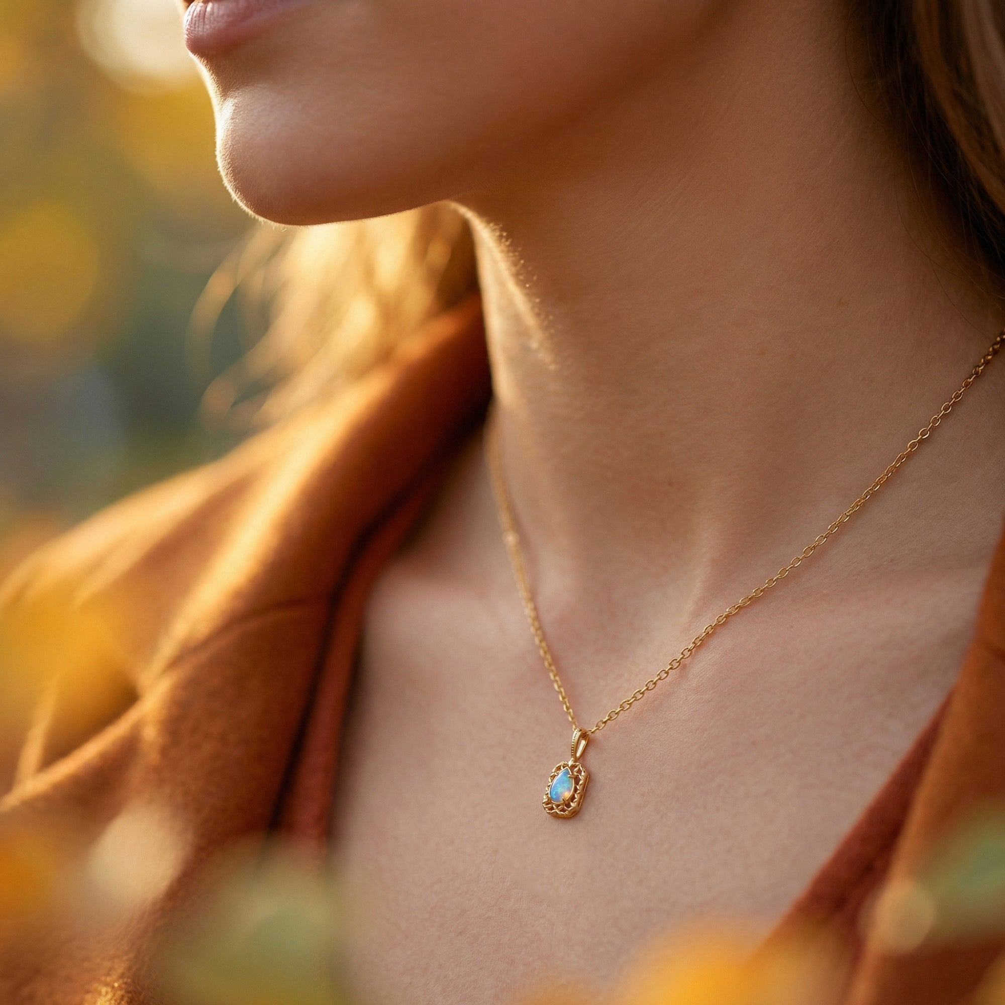 Side profile of a woman wearing the Avelina pear-cut opal necklace in gold finish in warm sunlight.