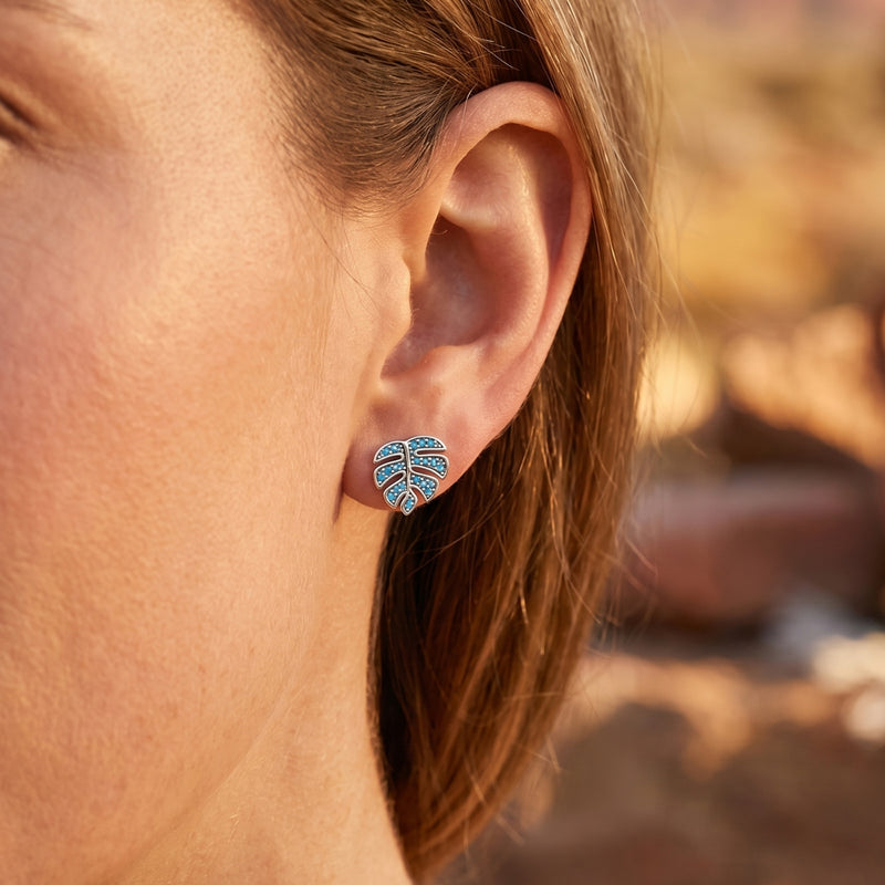 Close-up of a silver monstera leaf earring with turquoise stones worn on a woman's ear.