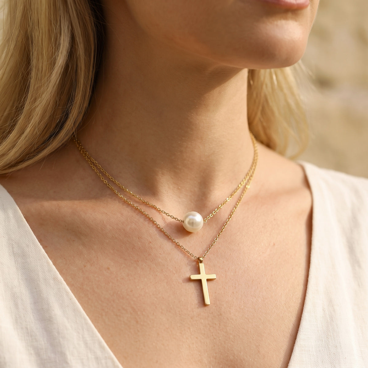 Angled close-up of a model wearing the gold-tone layered necklace with a pearl station and cross pendant.