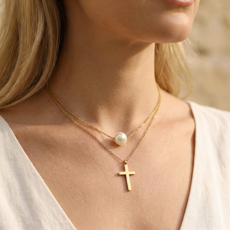 Angled close-up of a model wearing the gold-tone layered necklace with a pearl station and cross pendant.