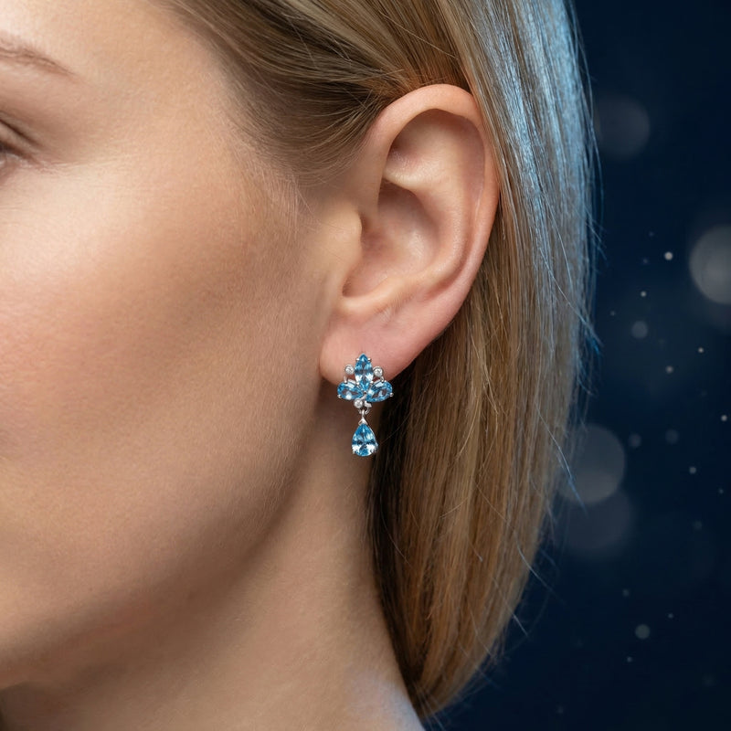 Woman wearing a silver drop earring featuring pear and marquise cut Swiss blue topaz stones.