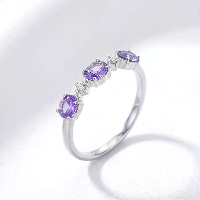 Angled side view of the Serenitas S925 sterling silver ring with oval simulated amethysts on white fabric.