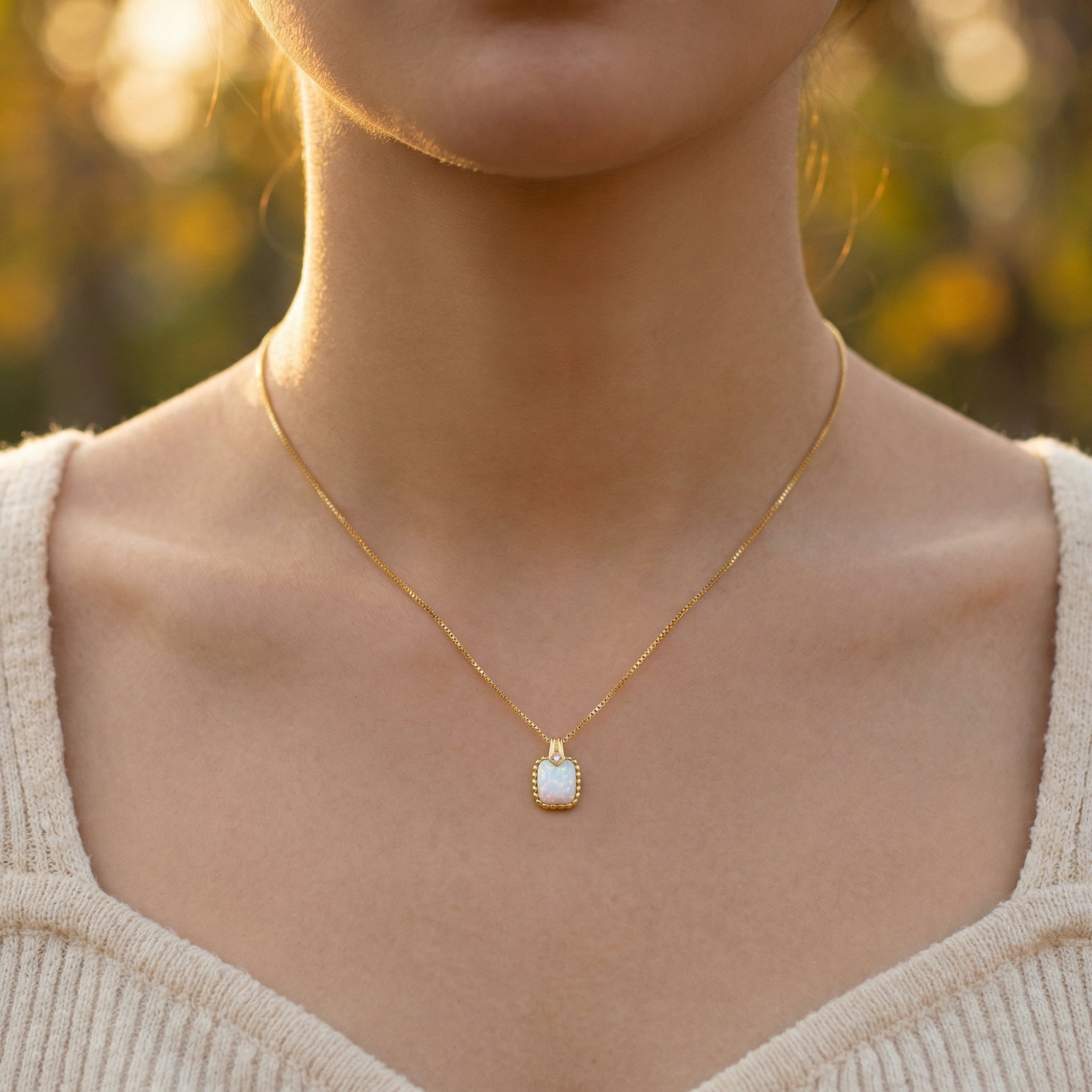 Model wearing the gold cushion cut white opal pendant necklace against a soft outdoor background.