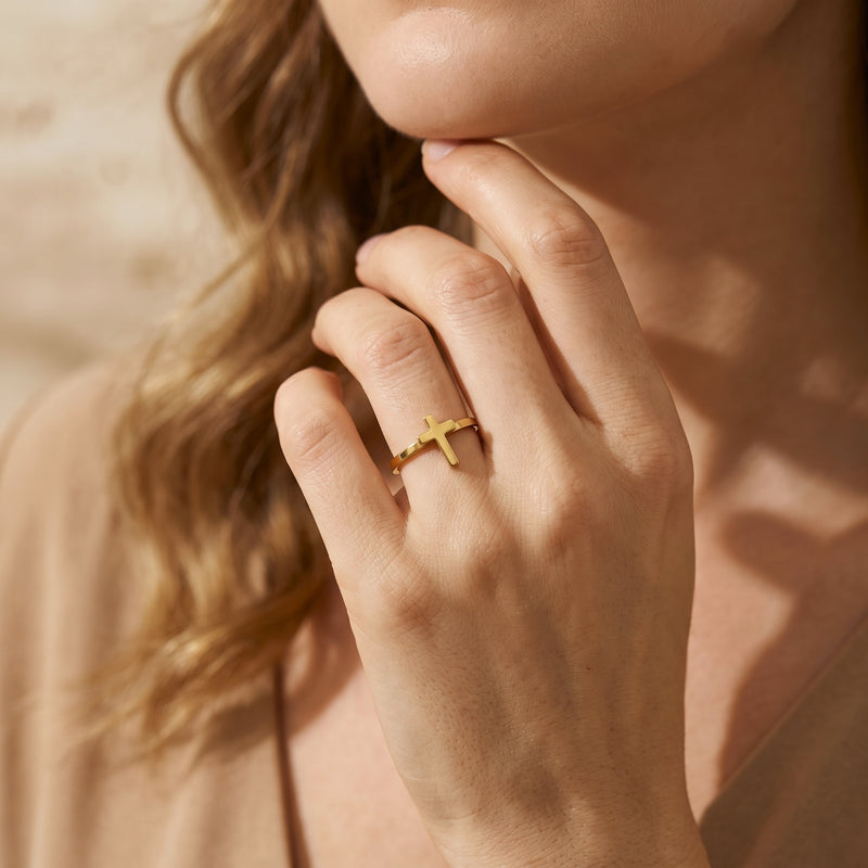 Model wearing the gold-tone cross ring on her finger, resting her hand near her chin.