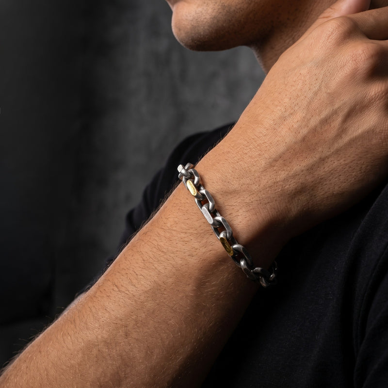 On-model view of a man wearing the silver heavy link chain bracelet with gold-tone bar details.