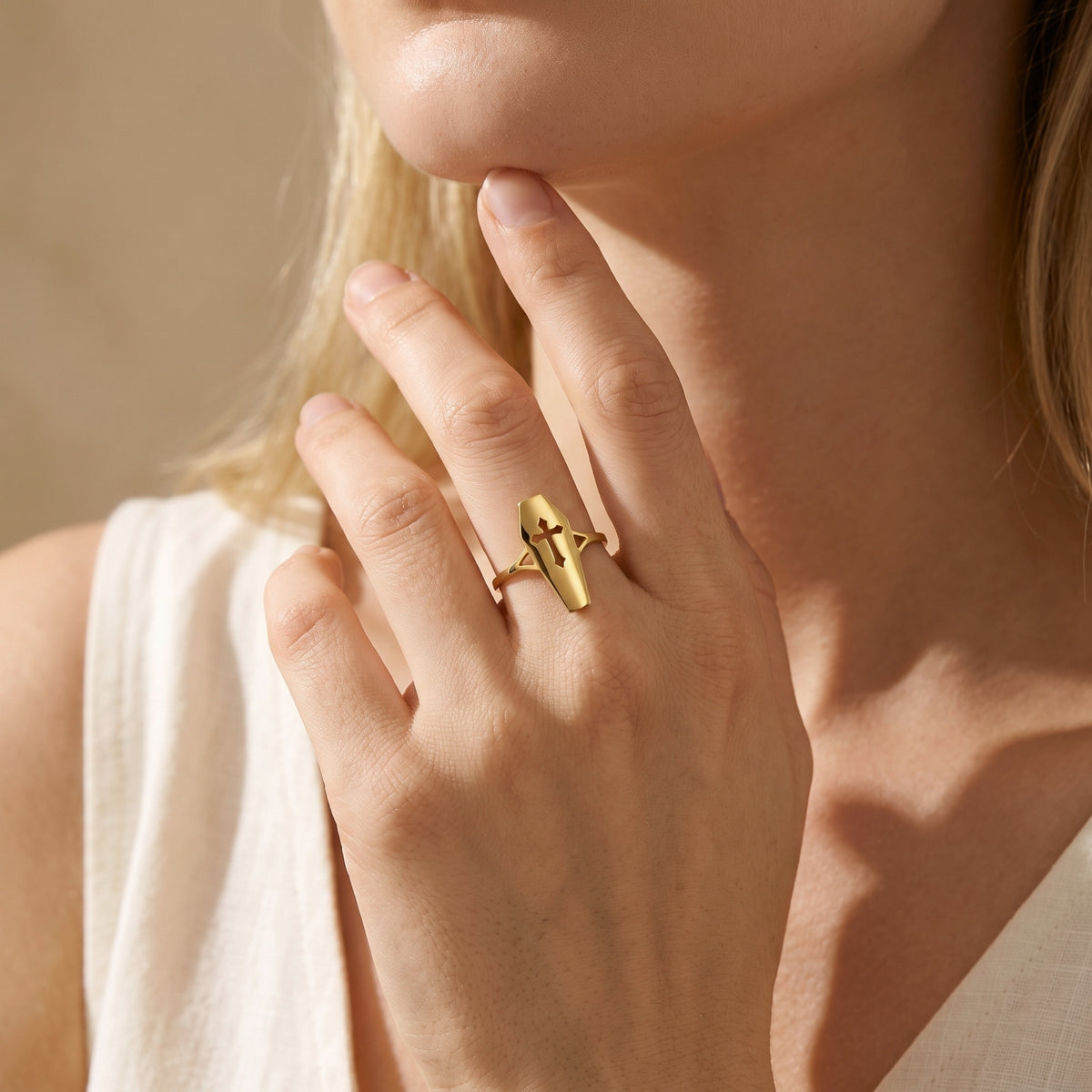 On-model view of a gold-tone coffin ring with a cutout cross worn on a raised hand.
