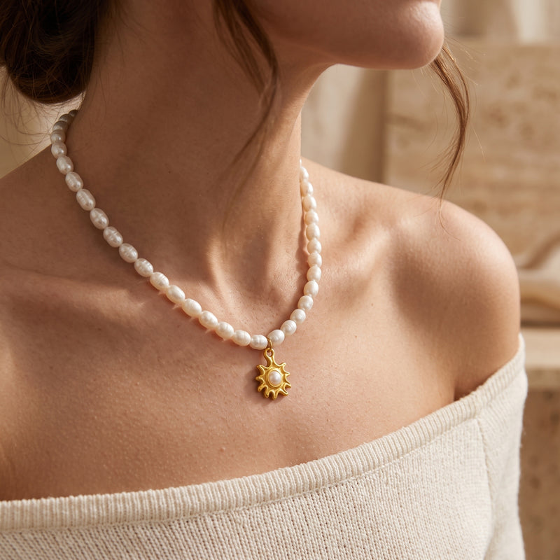 Model wearing the Solina pearl necklace with a gold sunburst pendant and white off-the-shoulder top.