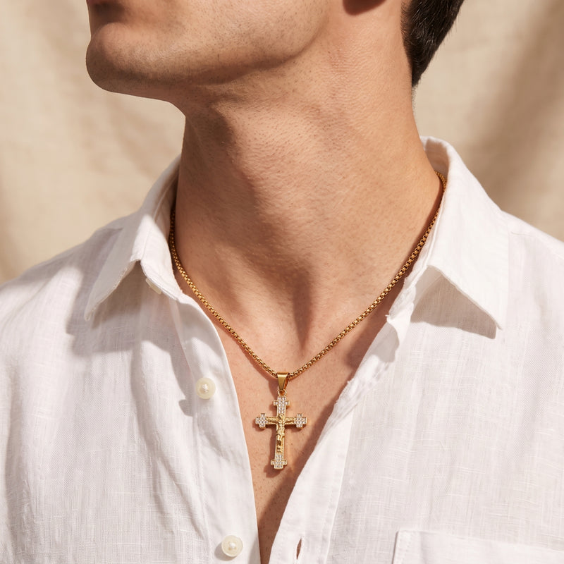 Model wearing a gold crucifix necklace with a box chain over an open white collared shirt.