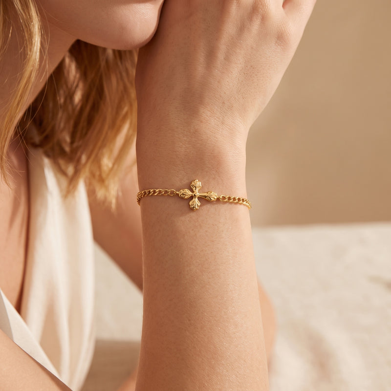 Gold-tone cross bracelet worn on a woman's wrist in a close-up lifestyle view.