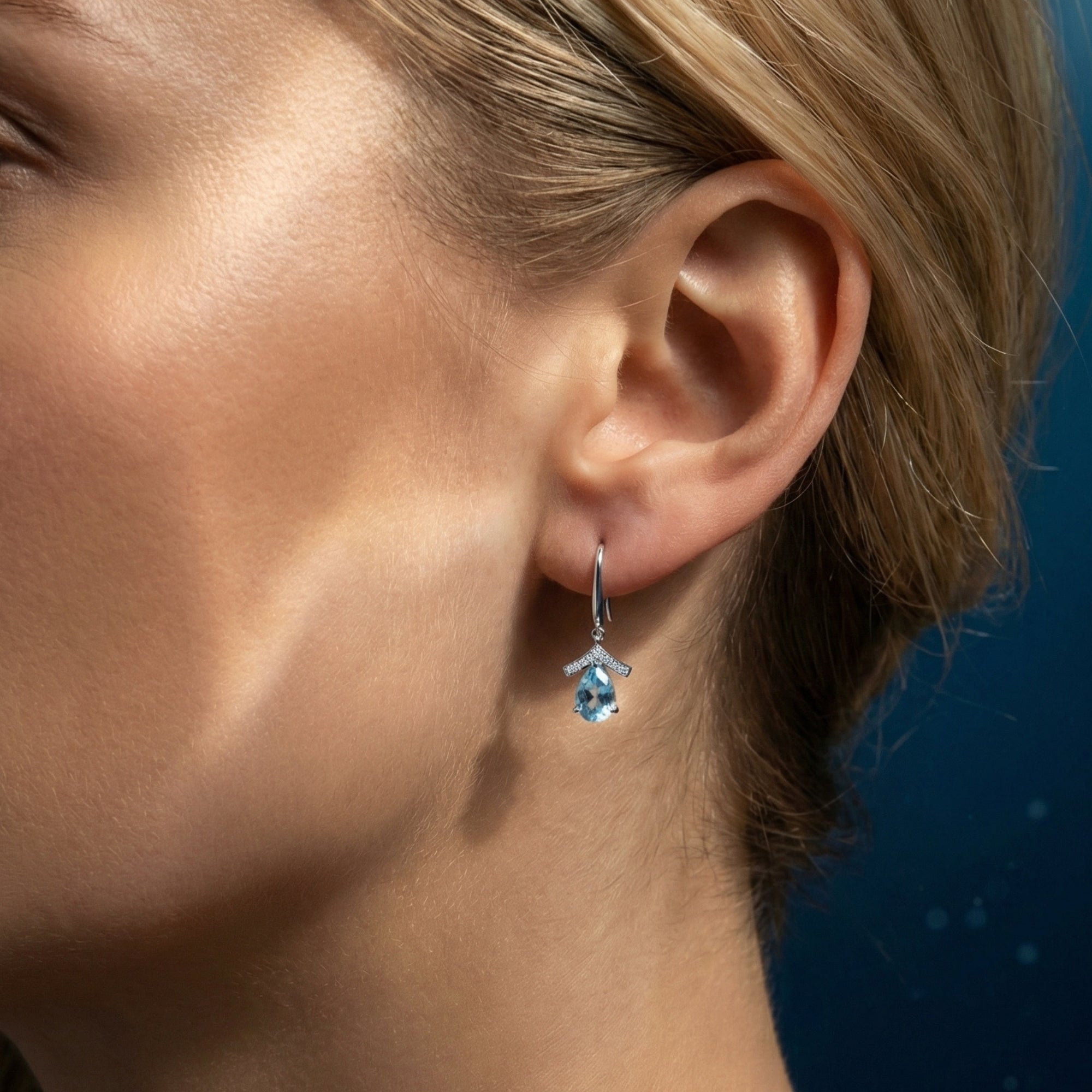 Woman wearing a pear cut natural aquamarine drop earring in platinum, showing how it hangs on the ear.