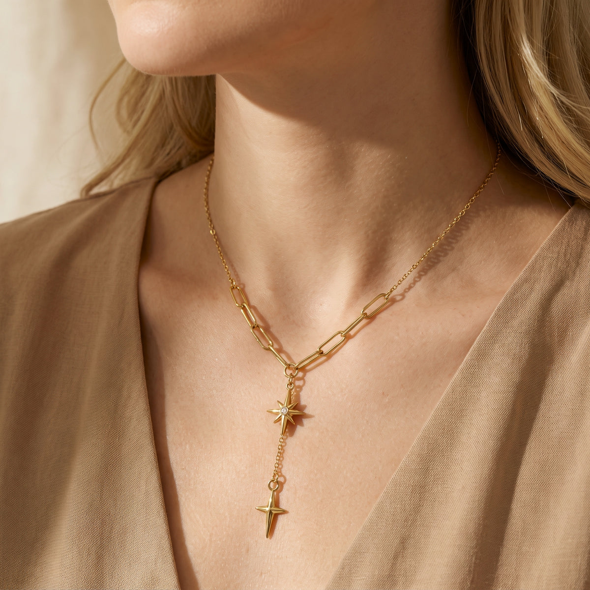 Close-up of a model wearing the gold-tone starburst lariat necklace over a beige V-neck garment.