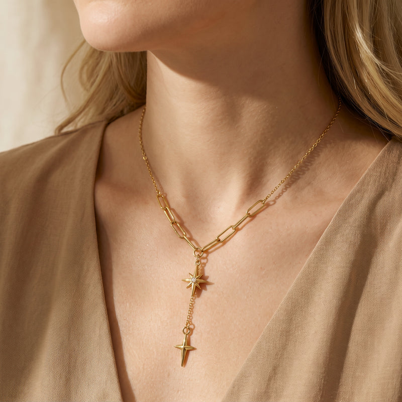 Close-up of a model wearing the gold-tone starburst lariat necklace over a beige V-neck garment.