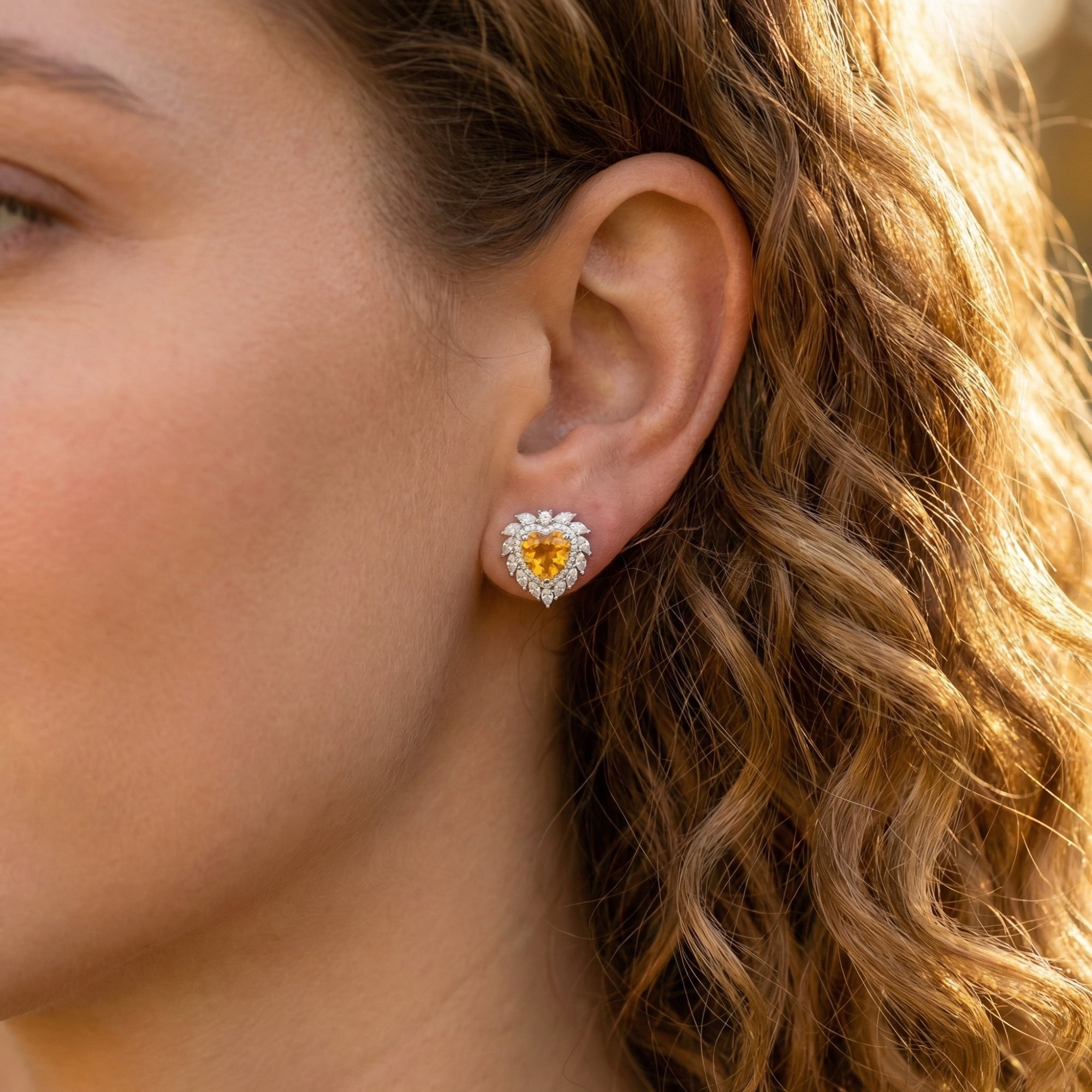 Model wearing a heart-cut natural citrine earring with a halo of clear stones in white gold.