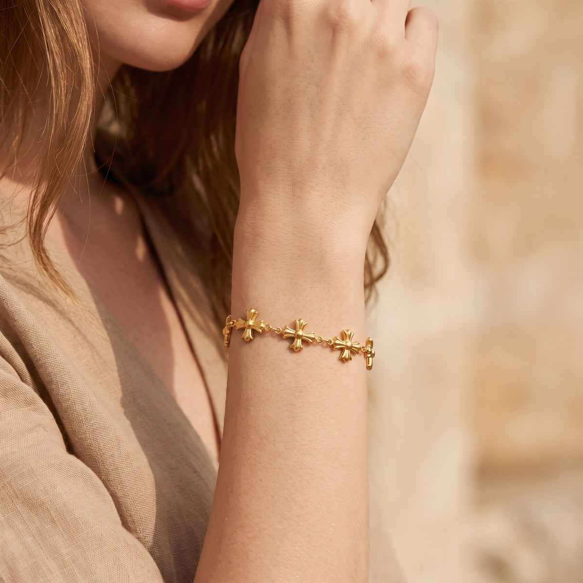 Model wearing the gold sculpted cross bracelet on her raised wrist in warm natural light.