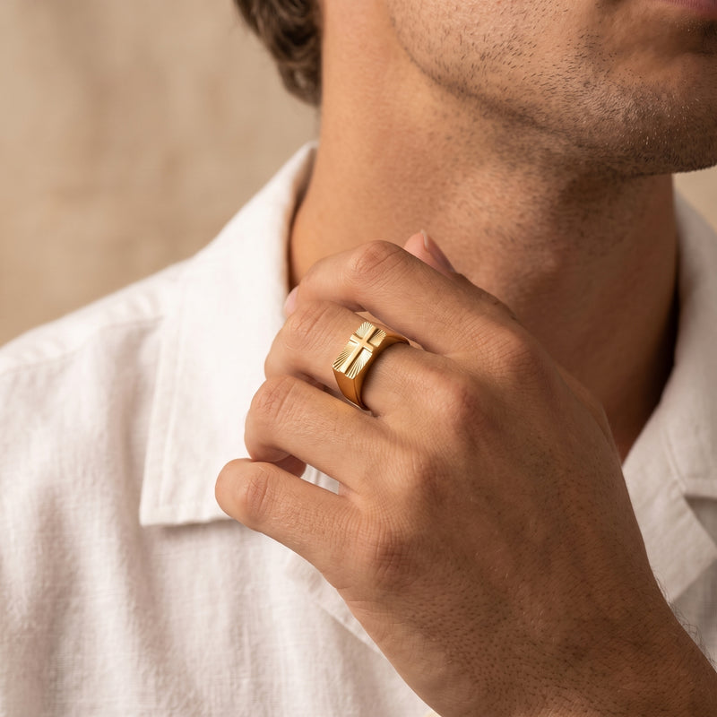 Close-up of a man wearing the gold-tone cross signet ring on his ring finger with a white shirt near his chin.