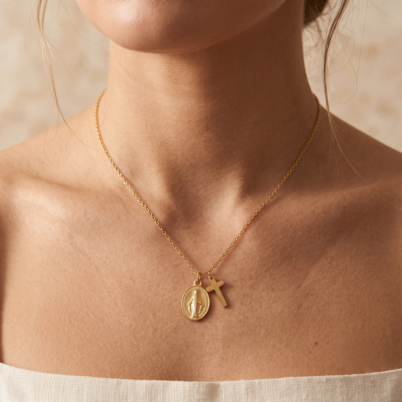 Close-up of a model wearing the gold-tone cross and oval medal necklace around her neck.