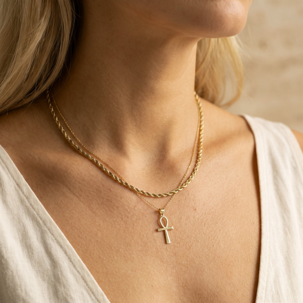 Side view of a woman wearing a layered gold-tone necklace with a rope chain and Ankh pendant.