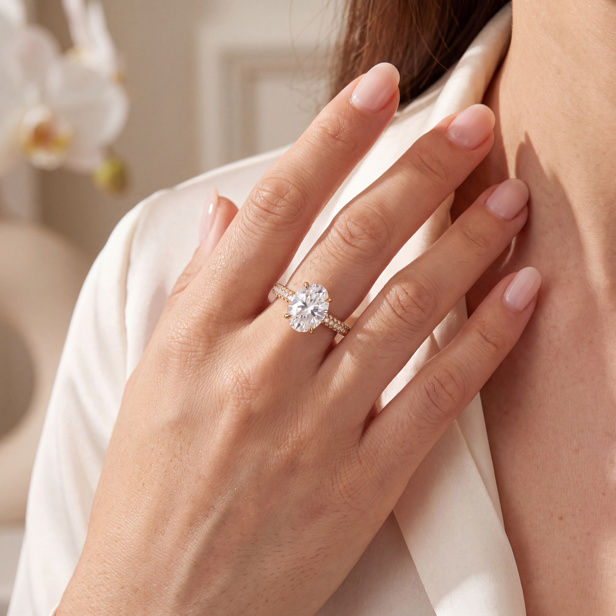 A model wearing an oval-cut moissanite engagement ring in yellow gold with a pavé band.